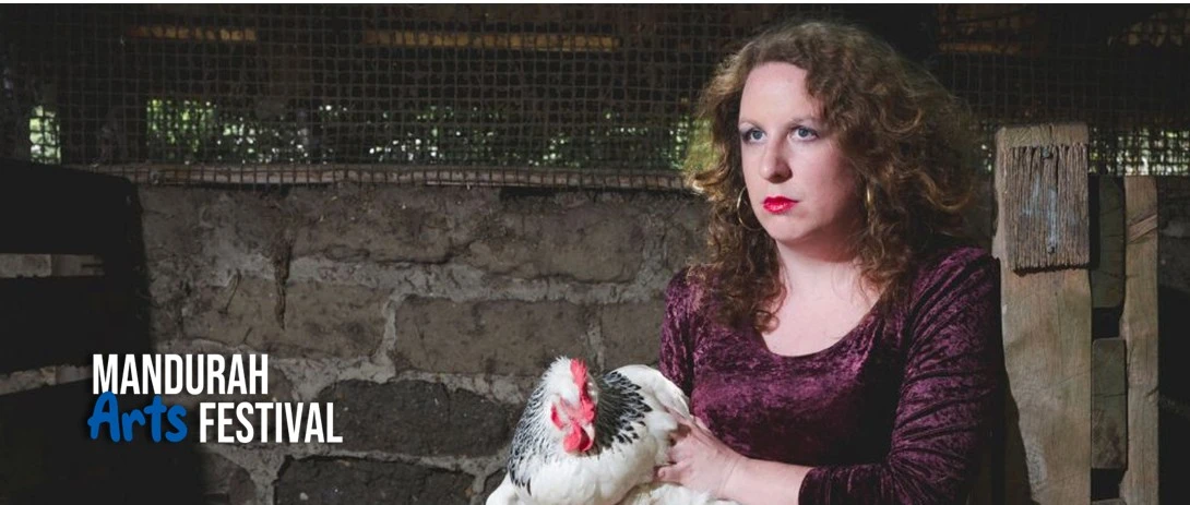 A woman wearing a purple velvet dress and a sour expression sits in a barn, holding a chicken